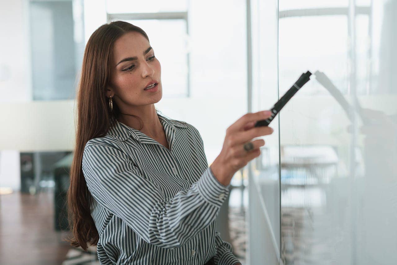 A focused businesswoman writing on a whiteboard during a presentation in a modern office.